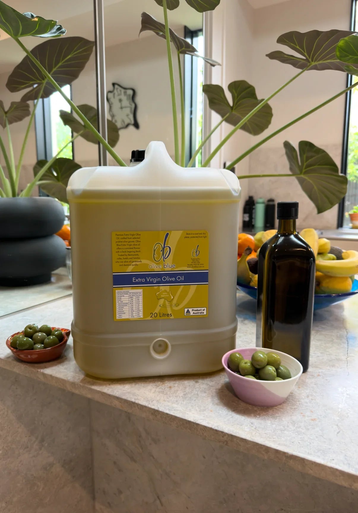 Large olive oil container, glass bottle, and bowls of green olives on a kitchen counter
